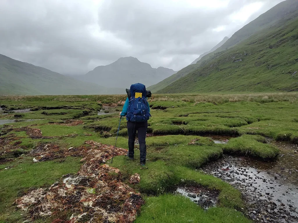 Solo backpacker trekking through a remote, rugged landscape in the Scottish Highlands, a perfect spot for wild camping in the UK.