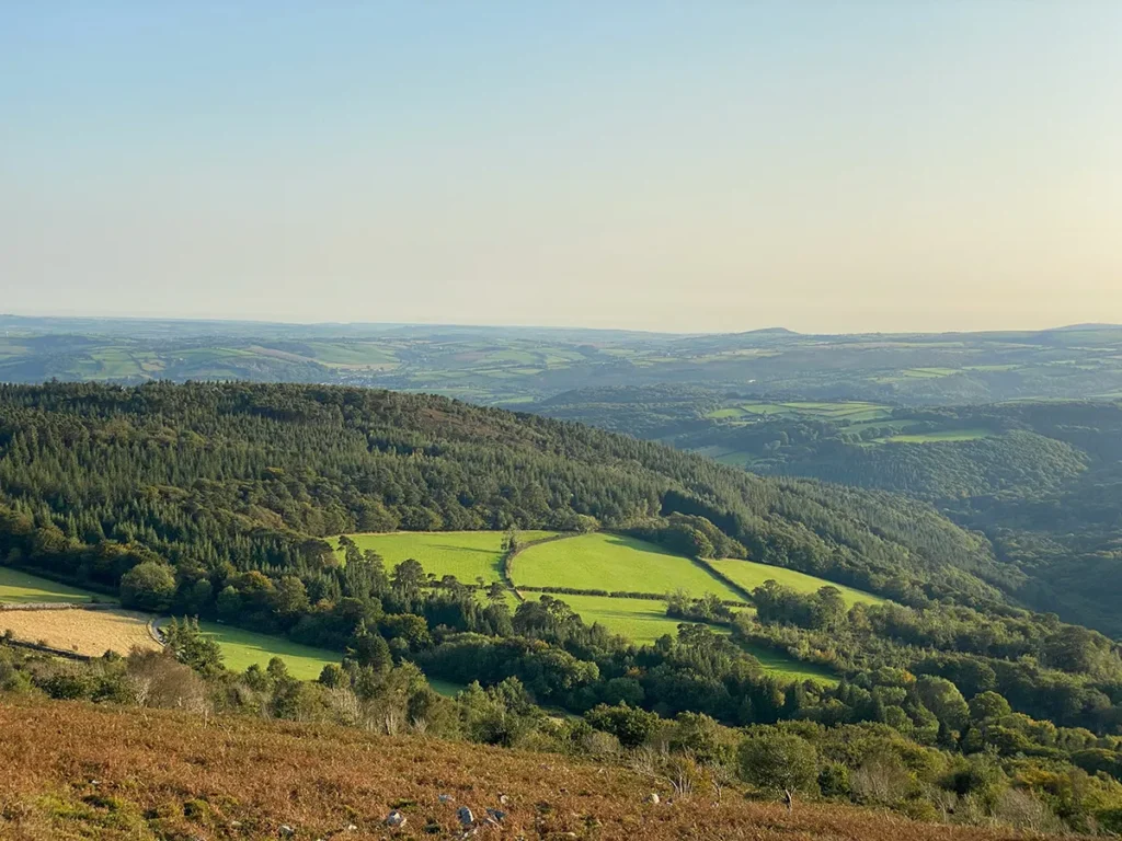 Expansive view of Exmoor National Park’s rolling hills and forests, a peaceful spot for wild camping in England.