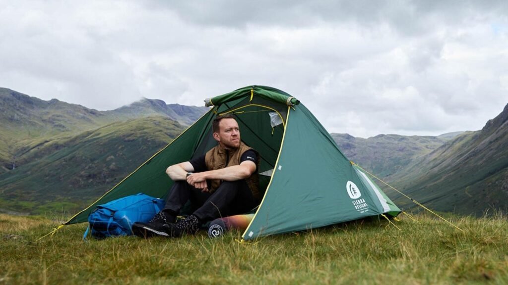 tent in field on top of hill with outdoorsy person sat inside