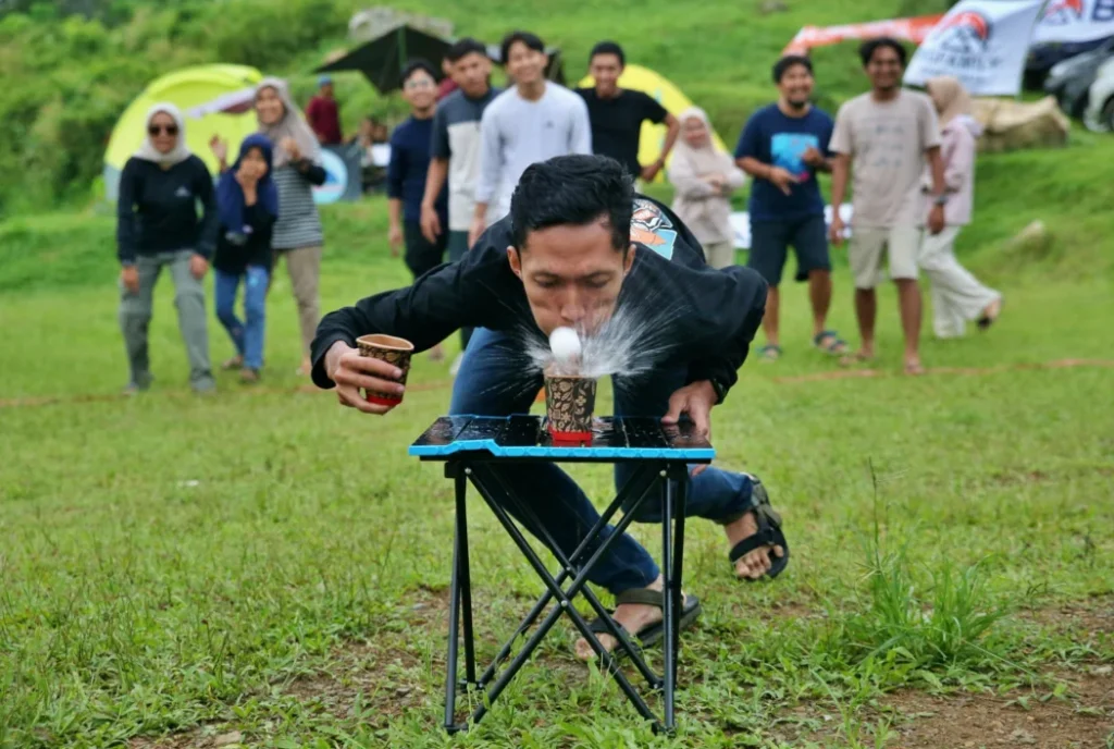 Camper taking part in a cup-and-ball game while friends watch at a group campsite.