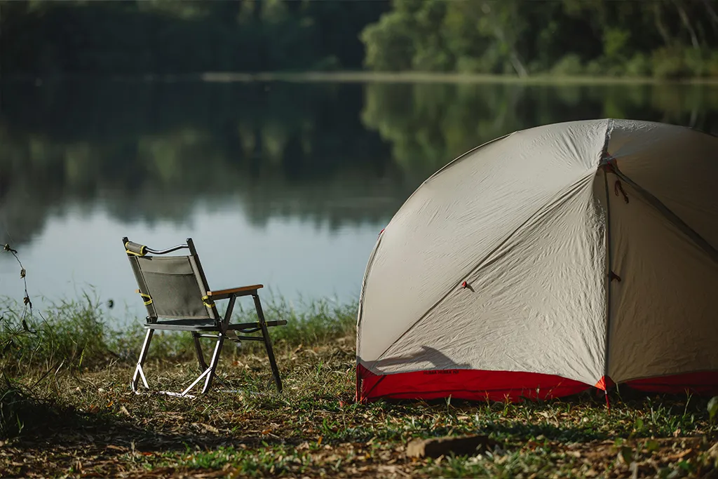 camping chair and tent next to a lake in a forest