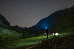 Person wearing a head torch while wild camping under a starry night sky in the mountains