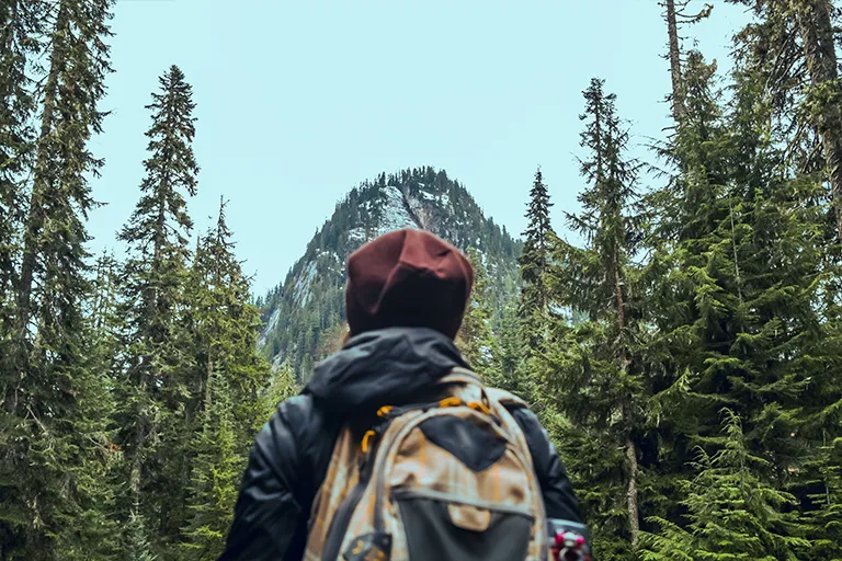 Woman hiking up mountain with a hat and backpack on