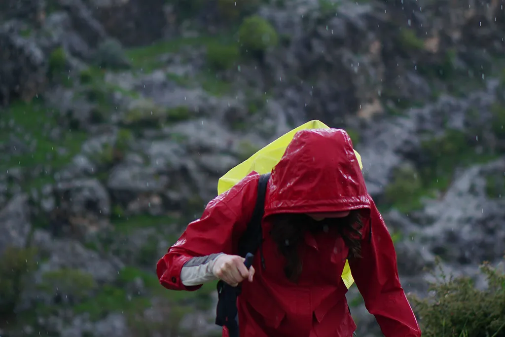 woman hiking in the rain up a hill with a red rain coat