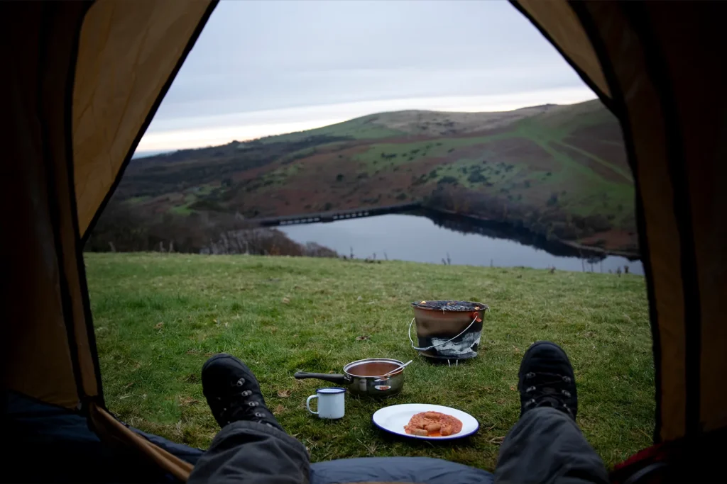View from inside a tent overlooking a lake and hills during a one-night wild camp in the UK