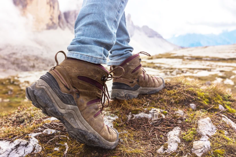 Hiker wearing well-used walking boots on rocky mountain terrain, illustrating footwear choice and blister prevention on hikes.
