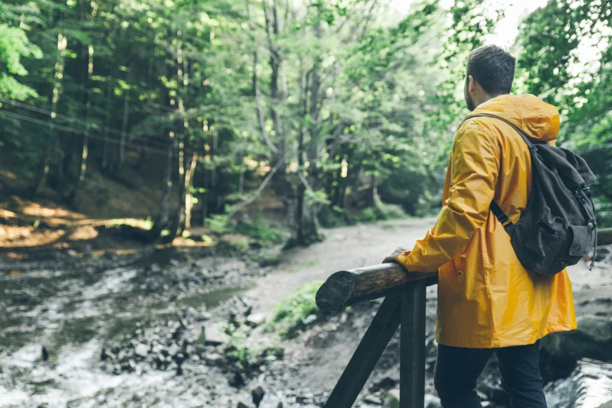 Hiker in a yellow waterproof jacket with a backpack walking through a wet woodland trail.