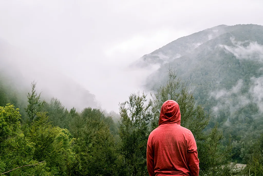 Hiking in a forest in an orange hoodie with fog surrounding the trees